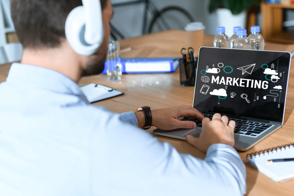 Cropped shot of businessman in headphones listening music and working at laptop with marketing word